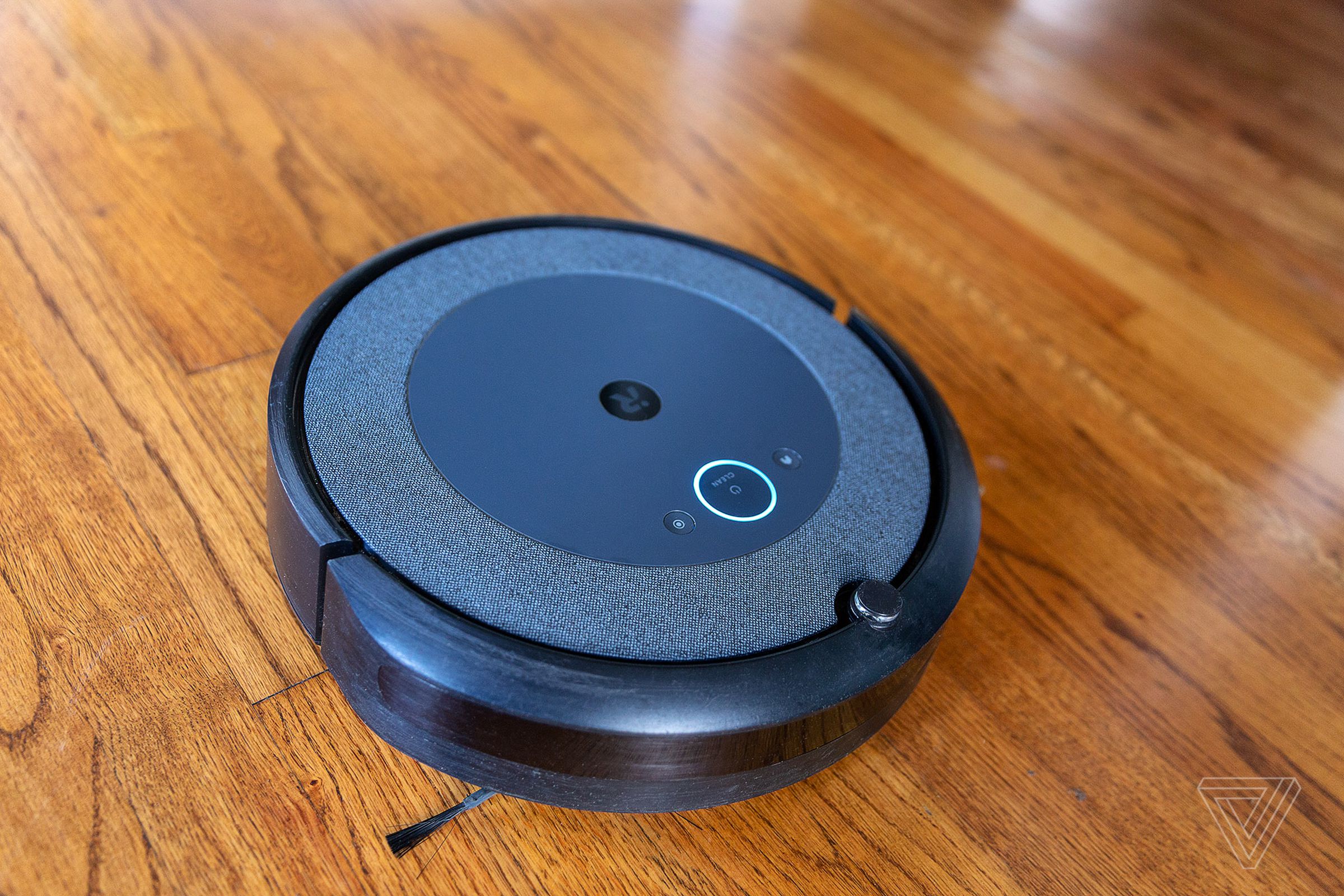 The iRobot Roomba i3 Plus EVO robot vacuum lying on a wooden floor.